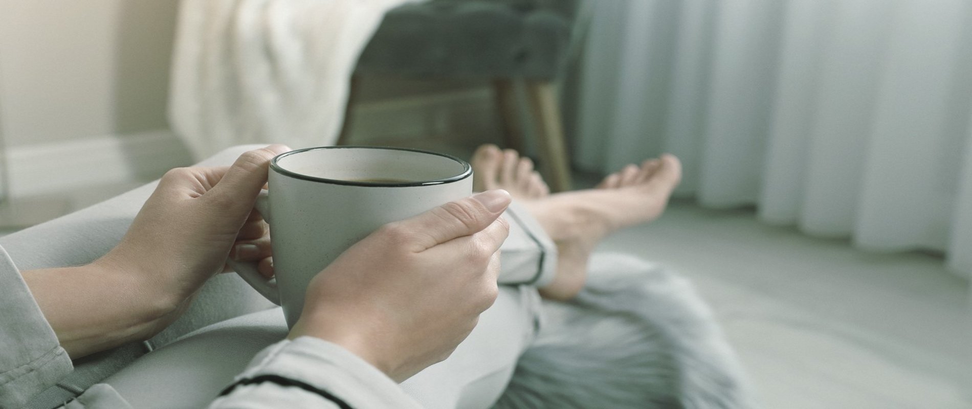 Eine Frau sitzt barfuß in einem Sessel, in ihren Händen hält sie eine Tasse