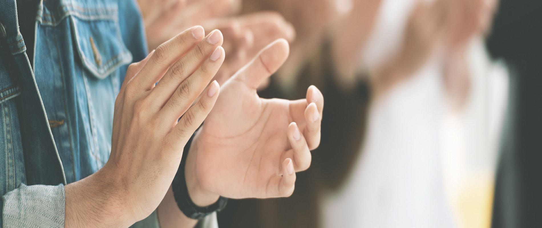 im Vordergrund sieht man zwei klatschende Hände, im Hintergund unscharf weitere klatschende Personen
